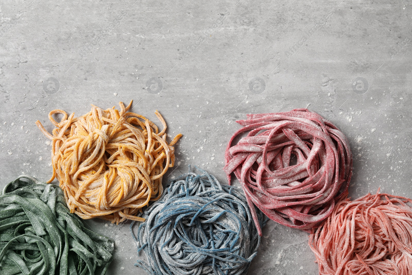 Photo of Rolled pasta painted with food colorings on light grey table, flat lay. Space for text