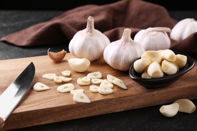 Aromatic cut garlic, cloves and bulbs on dark table, closeup