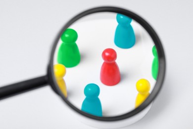 Photo of Magnifying glass over colorful pawns on white background. Recruiter searching employee