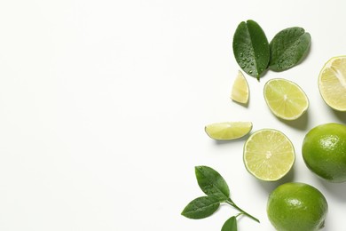 Whole and cut fresh ripe limes with green leaves on white background, flat lay