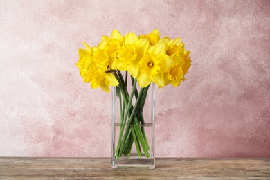 Photo of Bouquet of daffodils in vase on table against color background. Fresh spring flowers