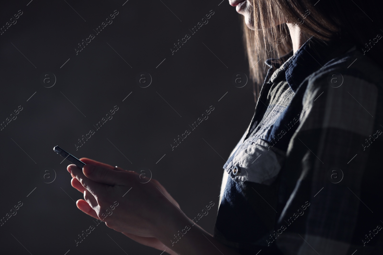 Photo of Woman using smartphone against dark background, closeup. Loneliness concept