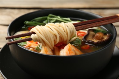 Photo of Bowl of delicious ramen with chopsticks on table, closeup. Noodle soup