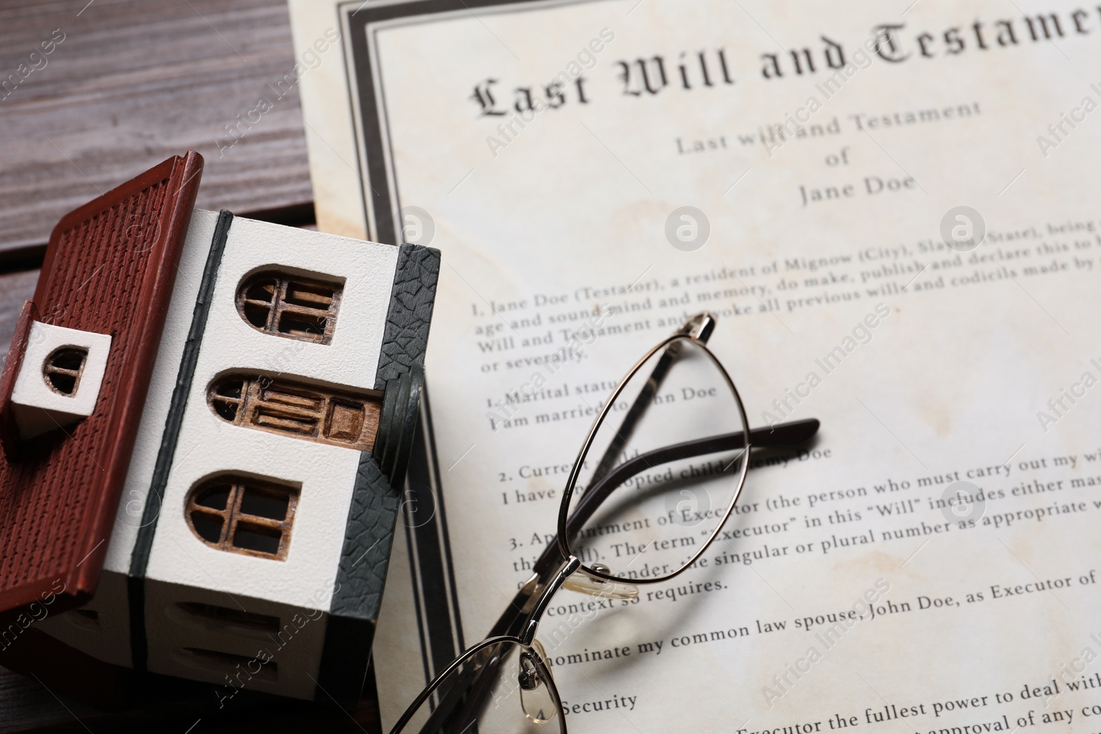 Photo of Last Will and Testament, house model and glasses on wooden table, closeup