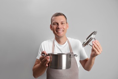 Photo of Happy man with cooking pot on light grey background