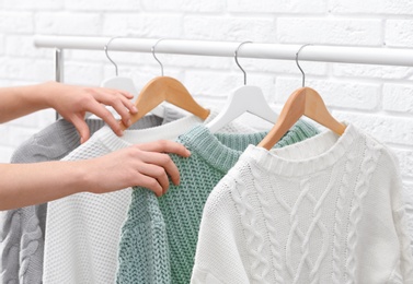 Photo of Woman choosing sweater on rack near brick wall, closeup