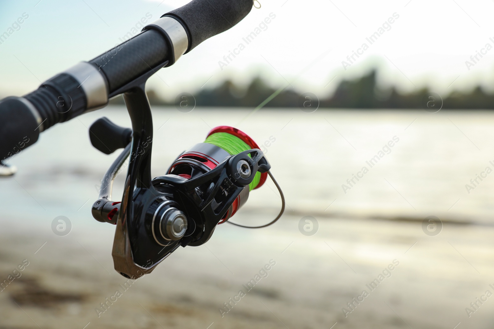 Photo of Fishing rod with reel near river, closeup. Space for text