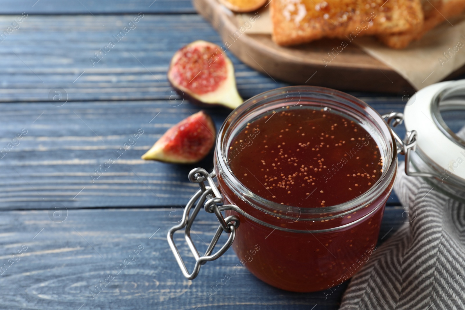 Photo of Delicious fig jam on blue wooden table, closeup. Space for text