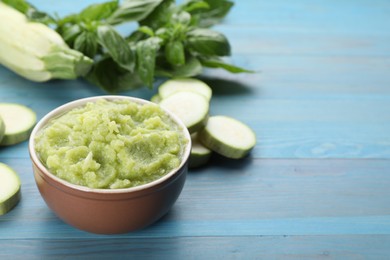 Photo of Bowl with green tasty puree, zucchini and basil on light blue wooden table. Space for text