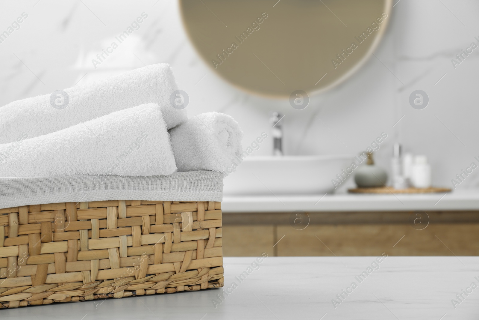 Photo of Wicker basket with rolled bath towels on white table in bathroom, space for text