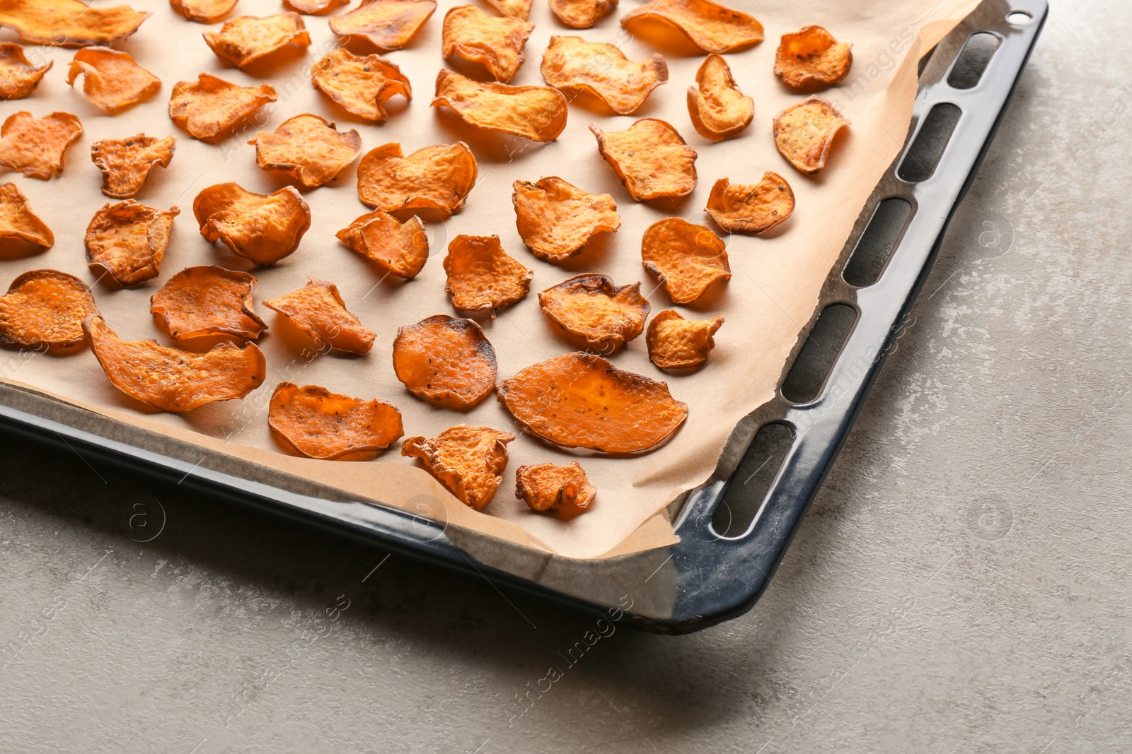 Photo of Baking sheet with sweet potato chips on grey background