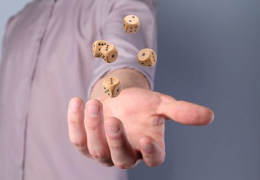 Man throwing wooden dice on grey background, closeup