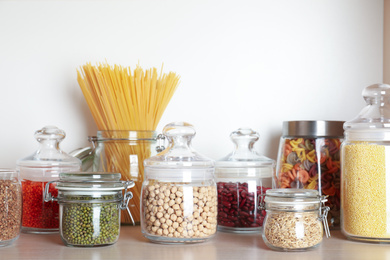 Photo of Glass jars with different types of groats on wooden shelf