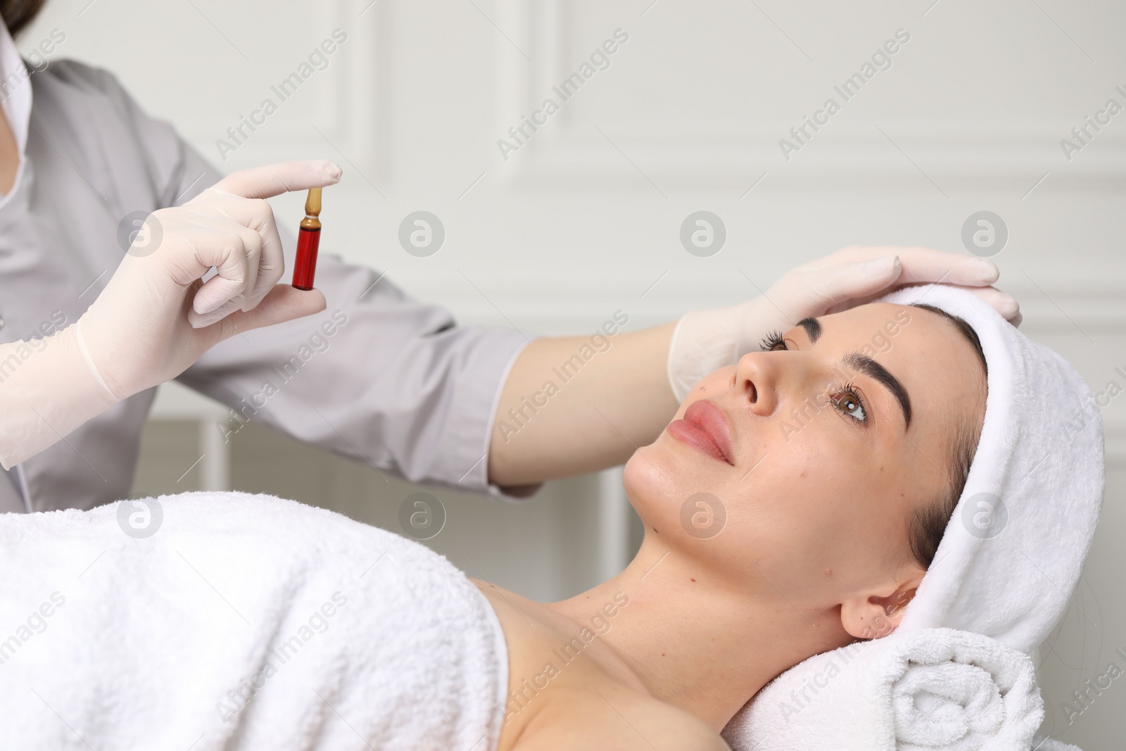 Photo of Professional cosmetologist holding skincare ampoule while working with client in clinic, closeup