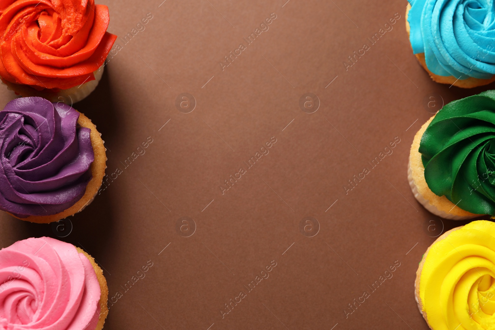 Photo of Delicious cupcakes with bright cream on brown background, flat lay. Space for text