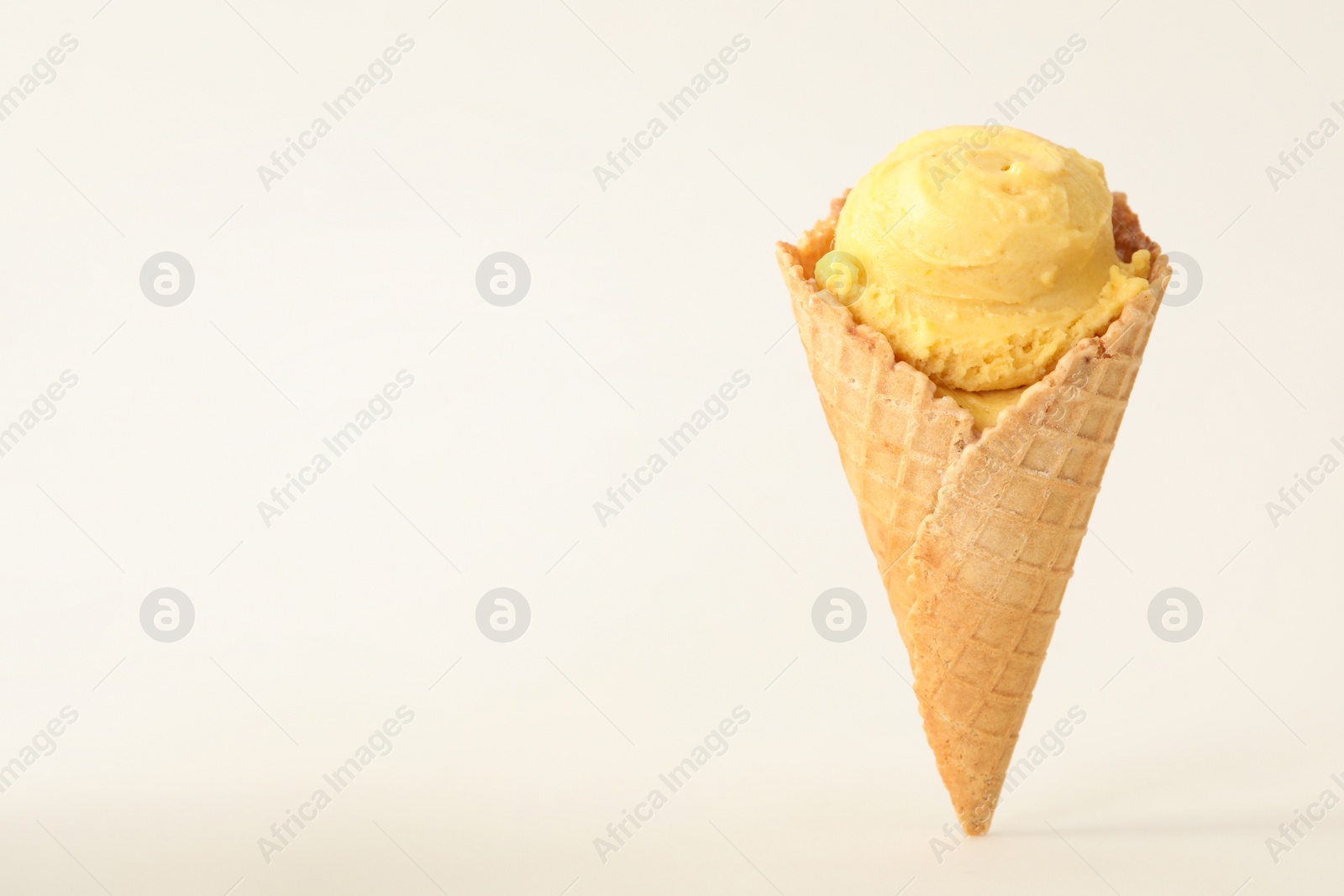Photo of Delicious yellow ice cream in waffle cone on white background. Space for text