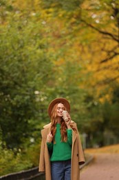 Photo of Beautiful woman drinking coffee from paper cup in autumn park. Space for text