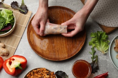 Photo of Woman making tasty spring roll at grey table, top view