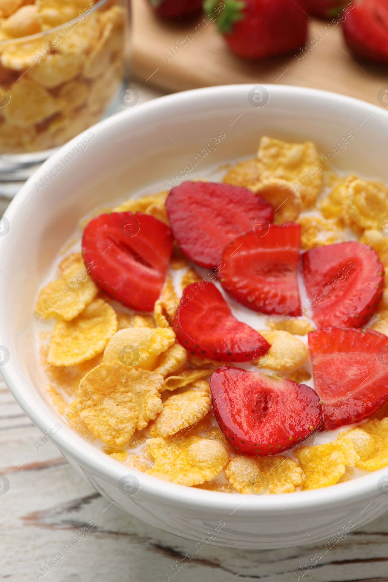 Photo of Bowl of tasty crispy corn flakes with milk and strawberries on white wooden table, closeup