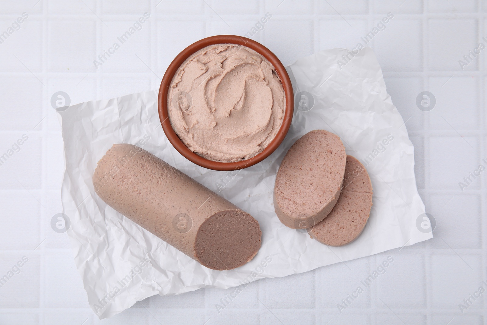 Photo of Delicious liver sausage and paste on white tiled table, flat lay