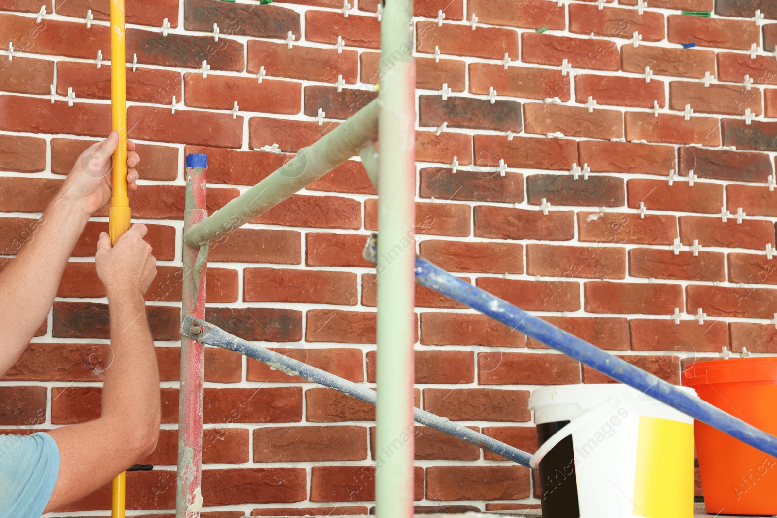 Photo of Professional builder working near brick wall, closeup. Tiles installation process