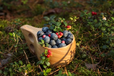 Wooden mug full of fresh ripe blueberries and lingonberries in grass