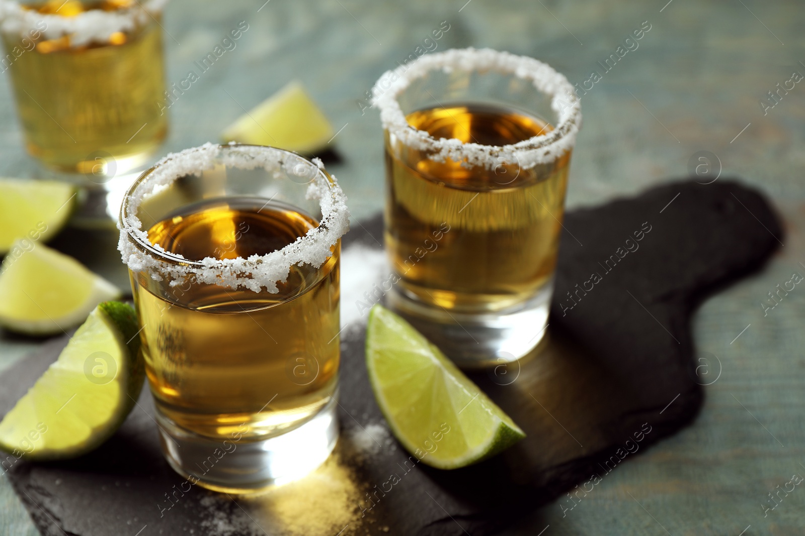 Photo of Mexican Tequila shots, lime slices and salt on blue wooden table