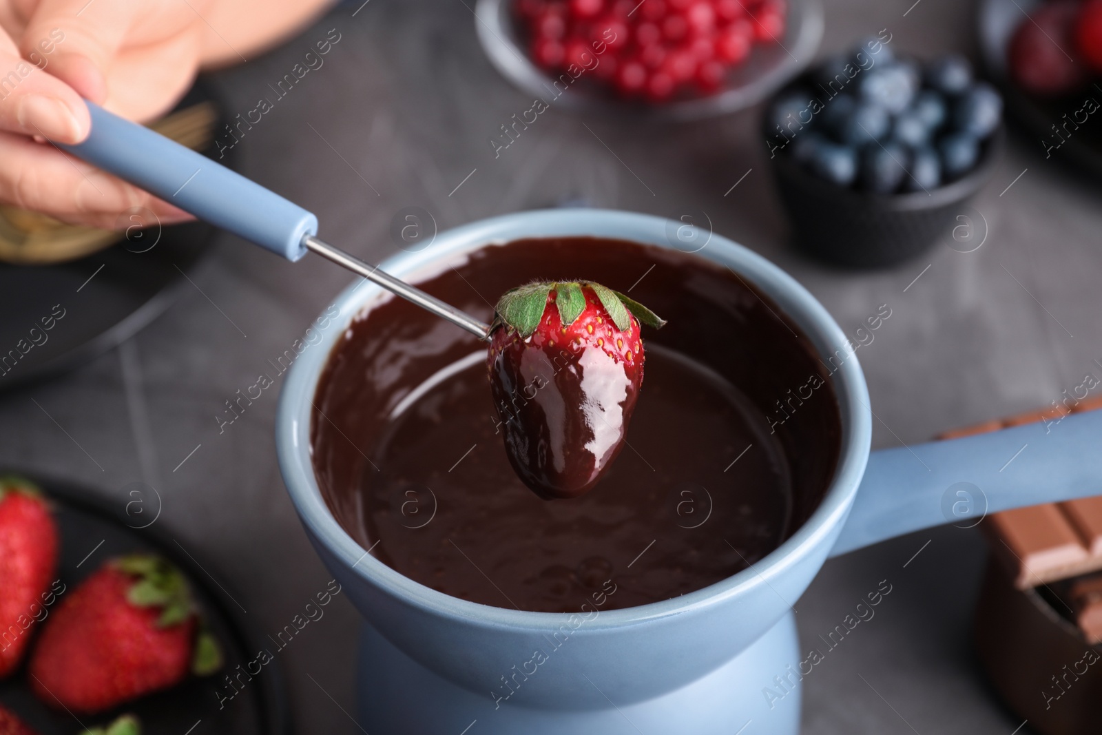 Photo of Woman dipping strawberry into pot with chocolate fondue at table, closeup