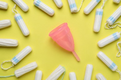 Photo of Menstrual cup and tampons on yellow background, flat lay