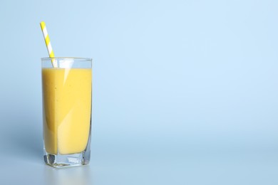 Glass of tasty smoothie with straw on light blue background. Space for text