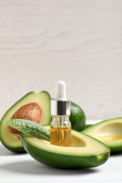 Photo of Essential oil and avocados on white table. Space for text