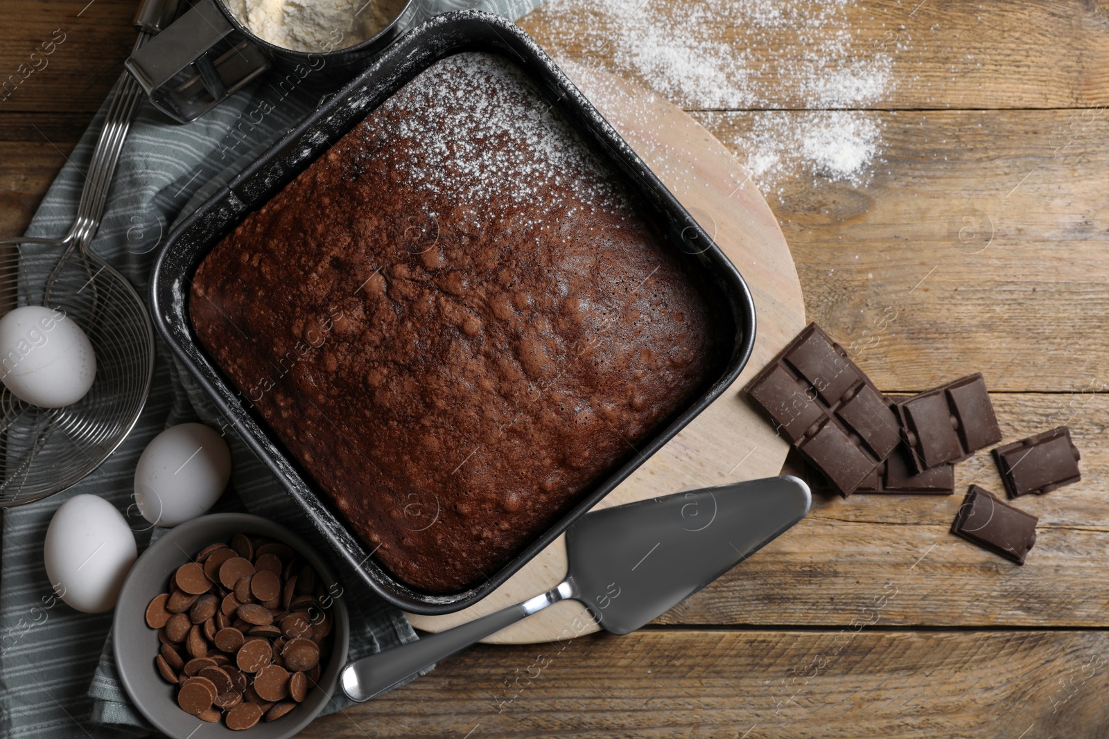 Photo of Homemade chocolate sponge cake and ingredients on wooden table, flat lay