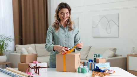 Photo of Beautiful young woman wrapping gift at table in living room