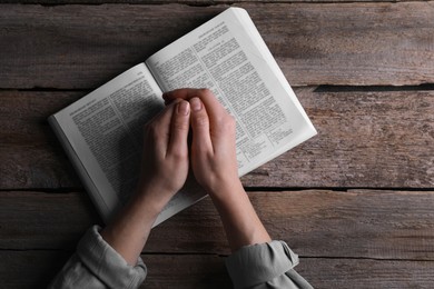 Photo of Religion. Christian woman praying over Bible at wooden table, top view. Space for text