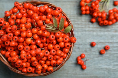 Photo of Fresh ripe rowan berries with leaves in wicker bowl on grey table, top view. Space for text