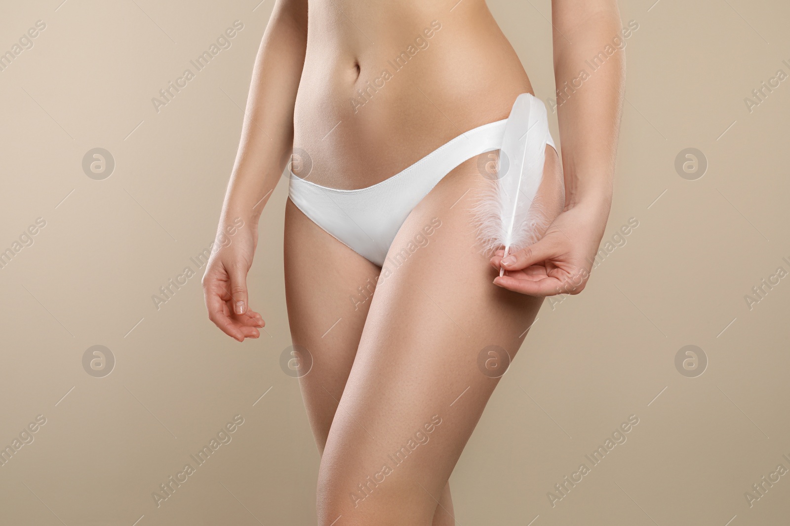 Photo of Woman with feather showing smooth skin on beige background, closeup. Brazilian bikini epilation