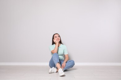 Photo of Young woman sitting on floor near light grey wall indoors