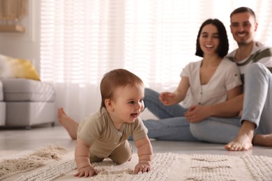 Happy parents watching their cute baby crawl on floor at home