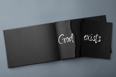 Image of Atheism as religious position. Torn paper with text God Exists in notebook on grey background, top view