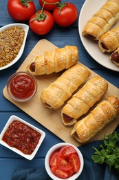 Photo of Delicious sausage rolls and ingredients on blue wooden table, flat lay