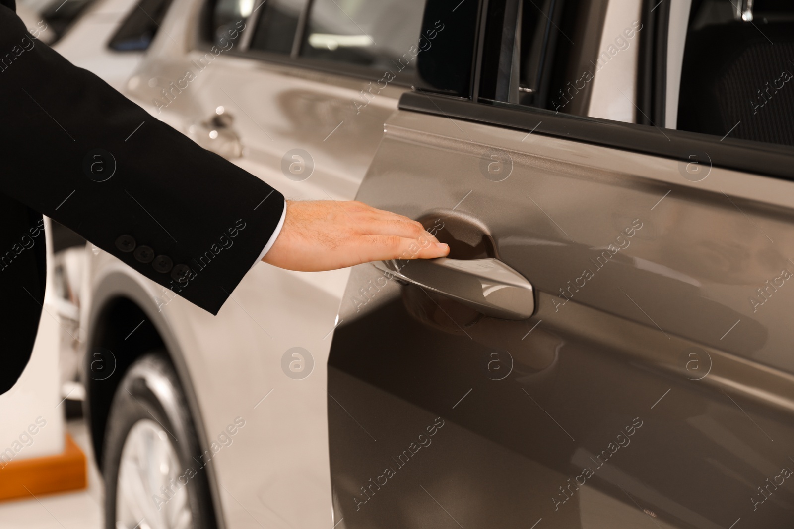 Photo of Young salesman in suit opening car door, closeup view