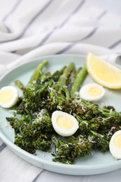 Tasty cooked broccolini with cheese, quail eggs and lemon on table, closeup