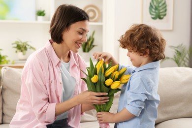 Photo of Happy woman with her cute son and bouquet of beautiful flowers at home. Mother's day celebration