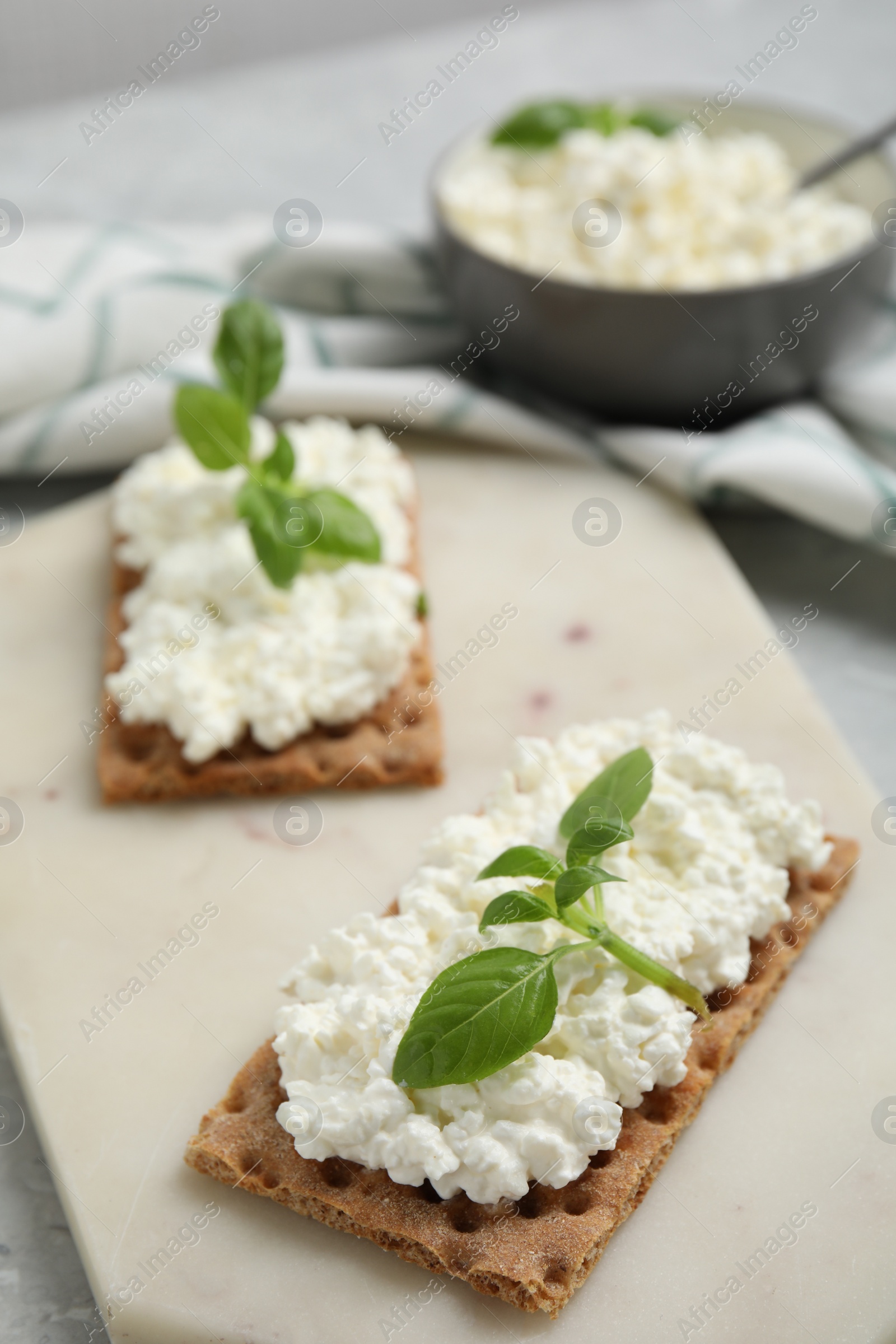 Photo of Crispy crackers with cottage cheese and basil on board, closeup