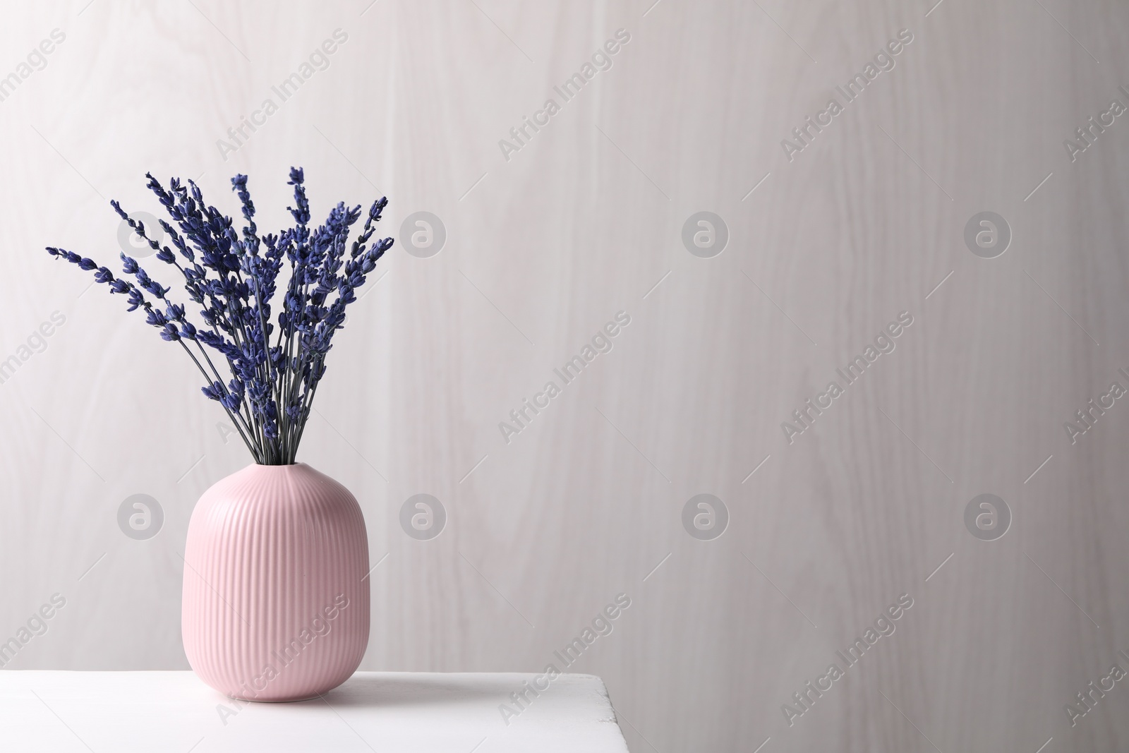 Photo of Bouquet of beautiful preserved lavender flowers on white table near grey wooden wall, space for text