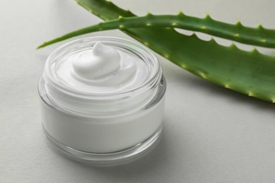 Jar with cream and aloe leaves on light grey background, closeup