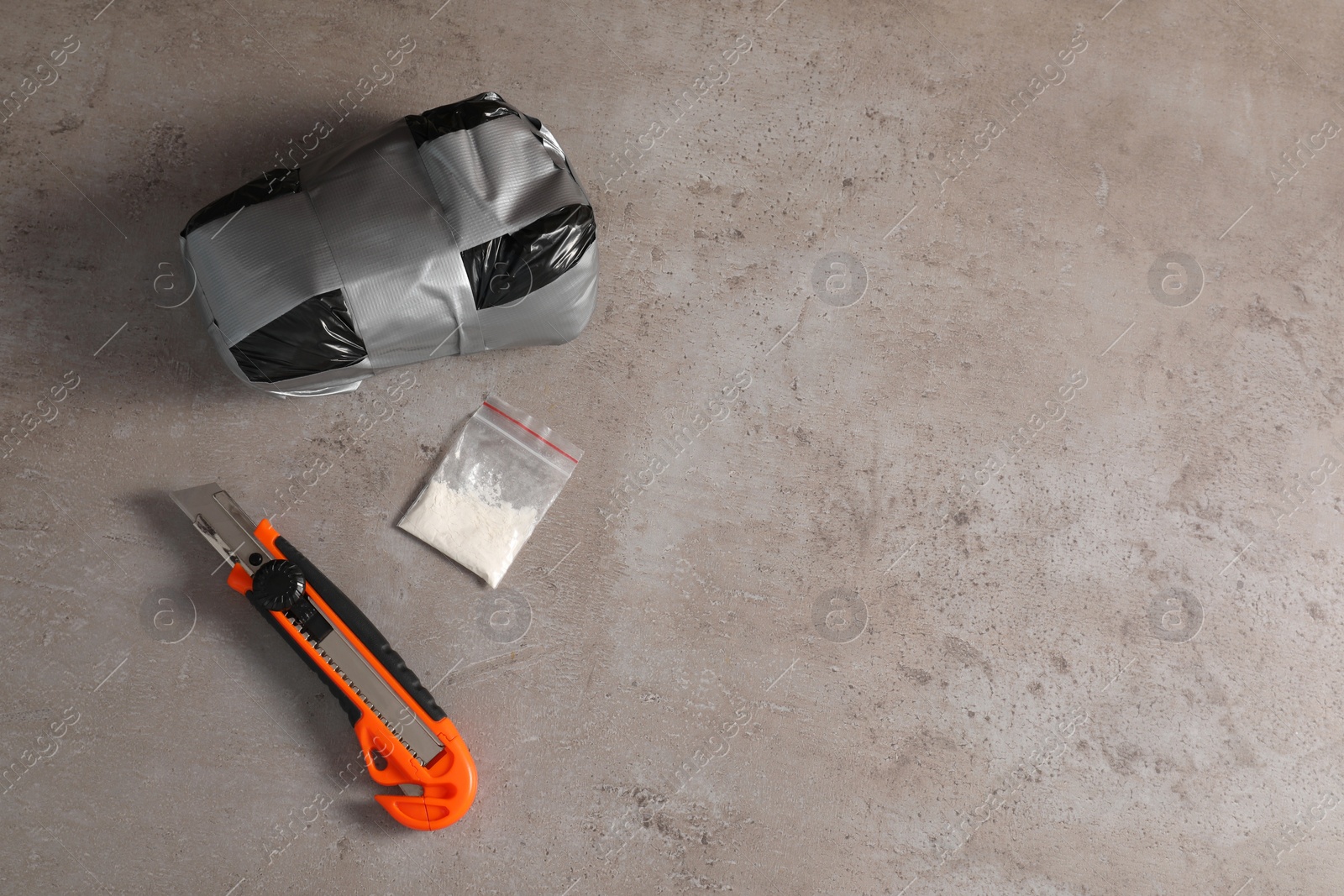 Photo of Packages with narcotics and stationery knife on grey textured table, flat lay. Space for text