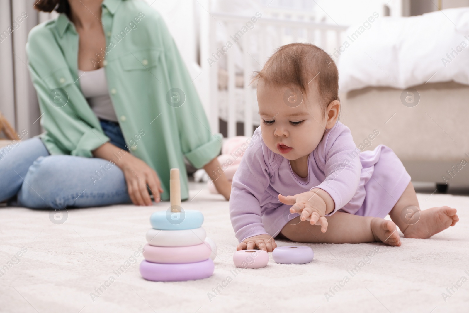 Photo of Cute baby girl playing with toy pyramid near mother on floor at home