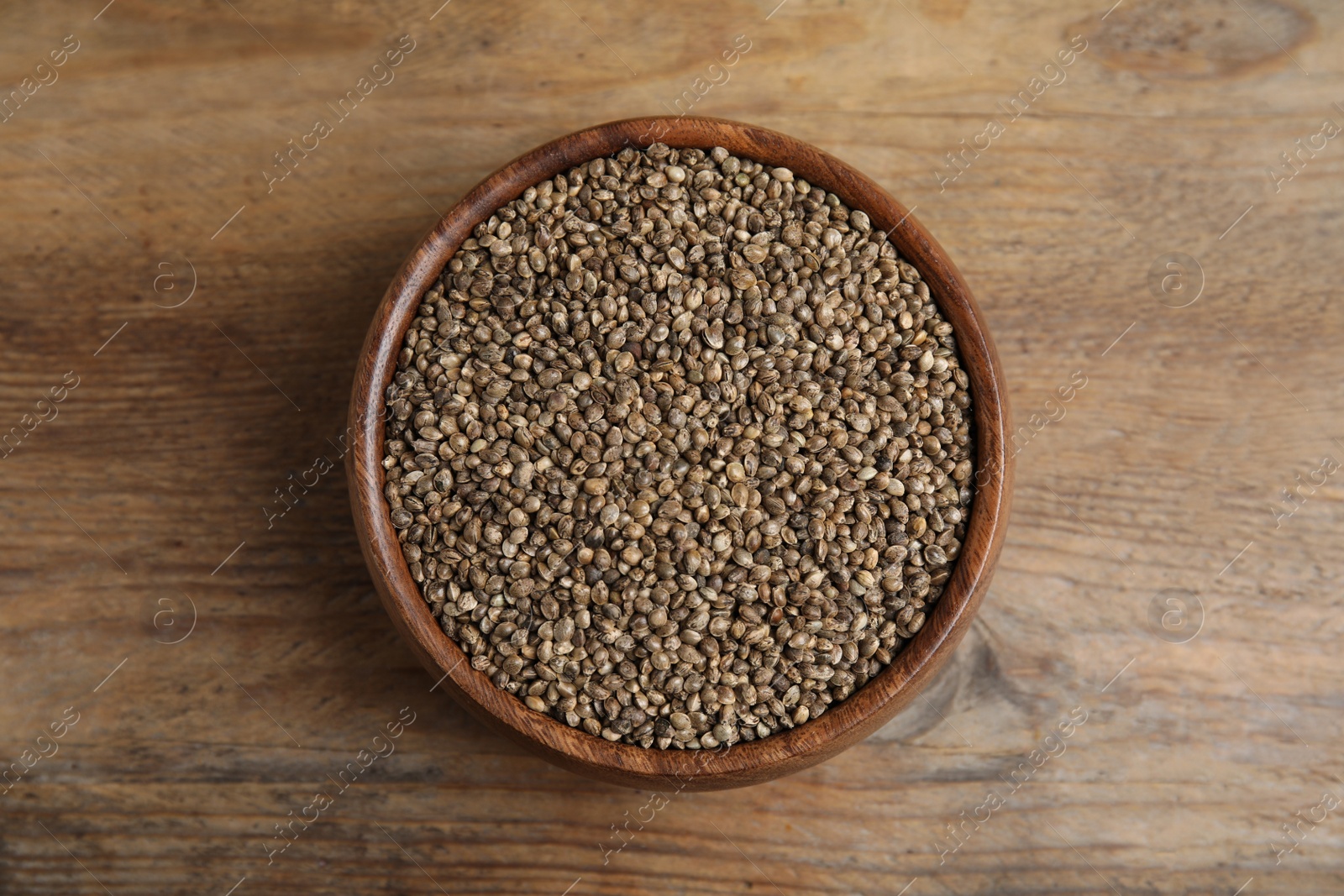 Photo of Bowl with organic hemp seeds on wooden table, top view