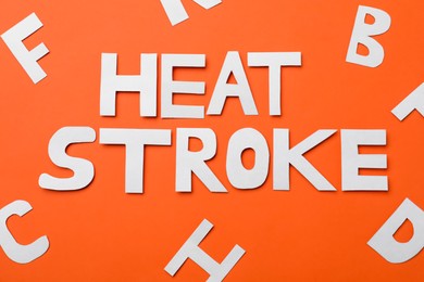 Photo of Words Heat Stroke made of paper letters on orange background, flat lay